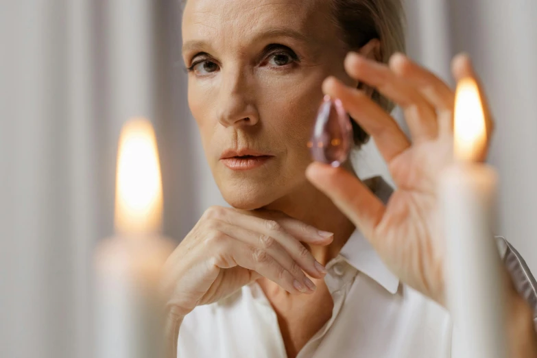 a woman holding candles in front of her face, by Julian Allen, trending on pexels, hyperrealism, pearl earring, offering the viewer a pill, older woman, gillian anderson