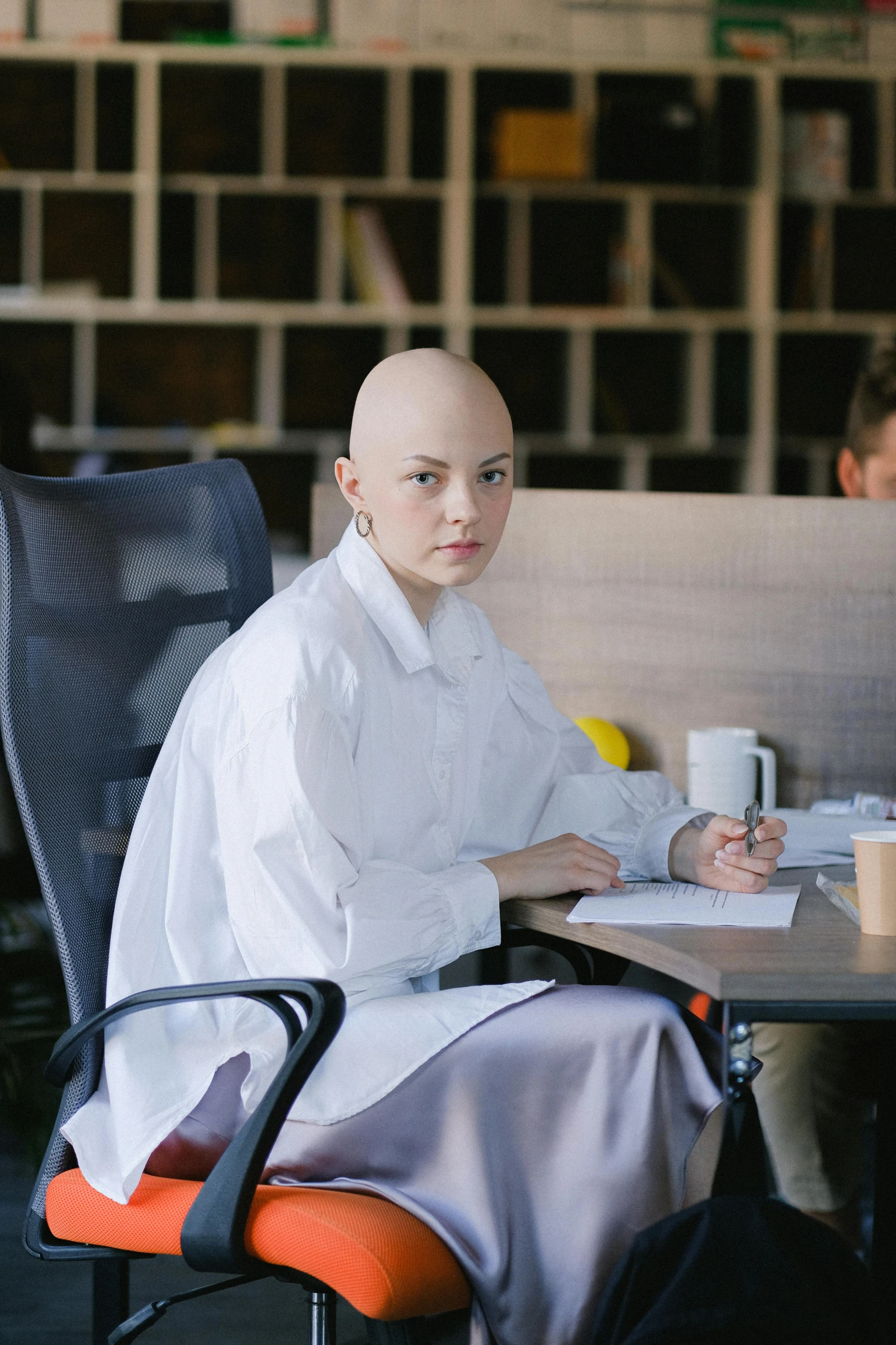 a bald man sitting at a desk in an office, by Julia Pishtar, trending on unsplash, renaissance, portrait androgynous girl, wearing a labcoat, ☕ on the table, photograph of a techwear woman