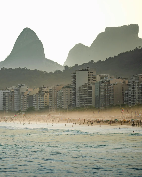 a man riding a surfboard on top of a wave in the ocean, by Elsa Bleda, mountains and a huge old city, oscar niemeyer, crowded beach, jen atkin