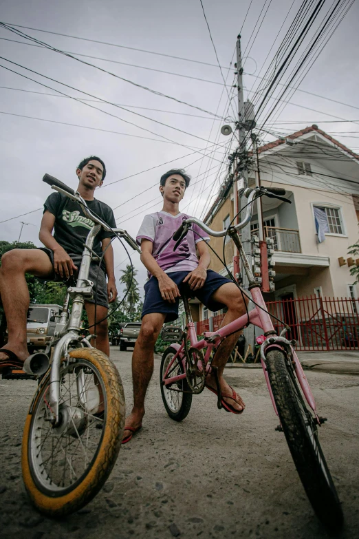 a couple of men riding bikes down a street, a portrait, by Jack C. Mancino, pexels contest winner, philippines, teenagers, in front of a garage, coloured photo