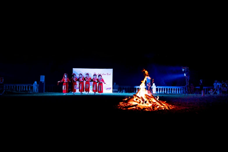 a group of people standing around a fire, by Jan Rustem, pexels contest winner, process art, assam tea garden setting, performing on stage, panoramic shot, ao dai