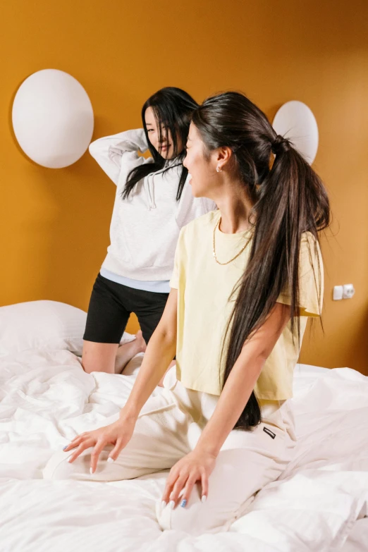 a couple of women standing on top of a bed, trending on pexels, happening, long black hair in a ponytail, bouncing, yellow hue, sweat