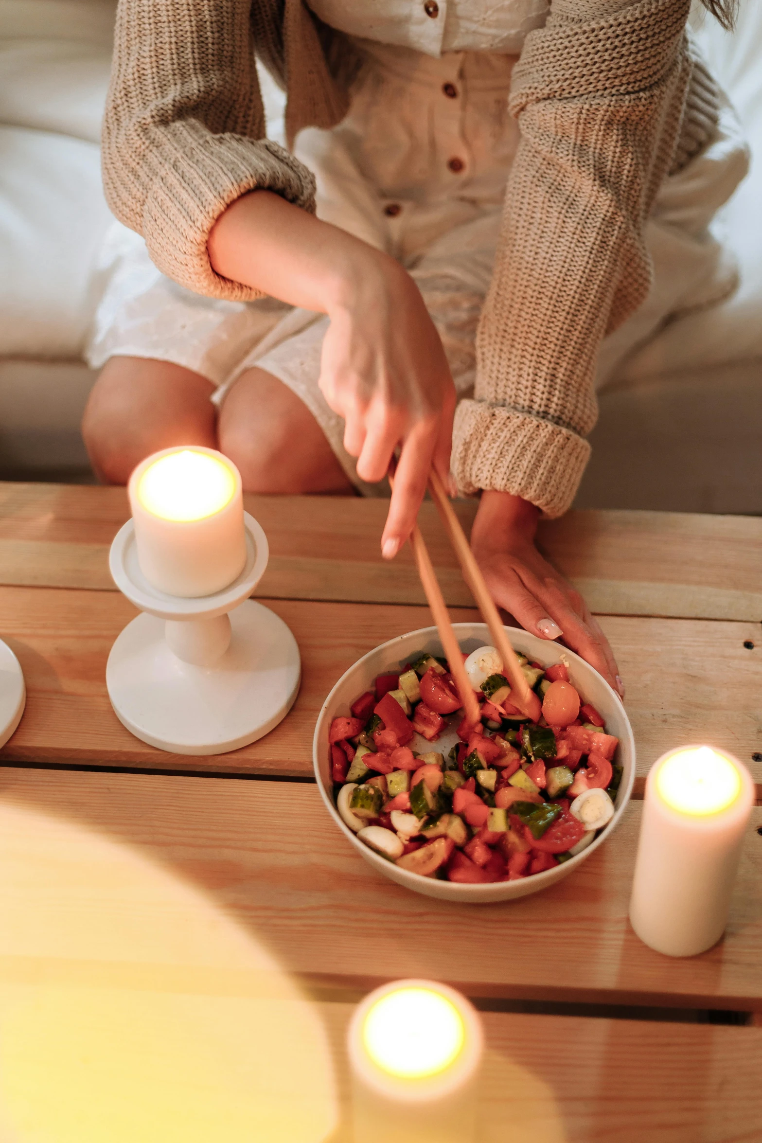 a woman sitting on a couch with a bowl of food, a still life, by Julia Pishtar, trending on pexels, the candle is on a wooden table, chopsticks, chopping hands, romantic lead