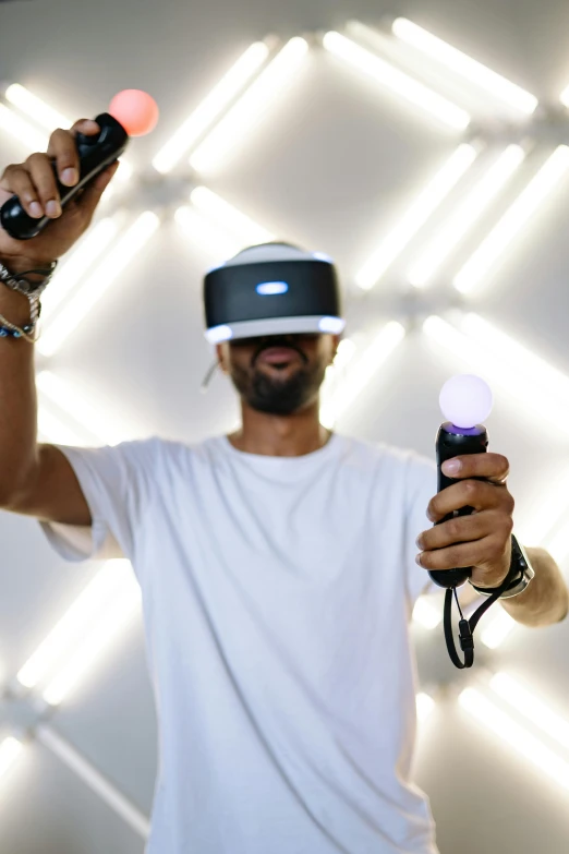 a man in a white shirt holding a nintendo wii controller, a hologram, unsplash, interactive art, floating vr headsets, shot with sony alpha, afro tech, vr helmet on man