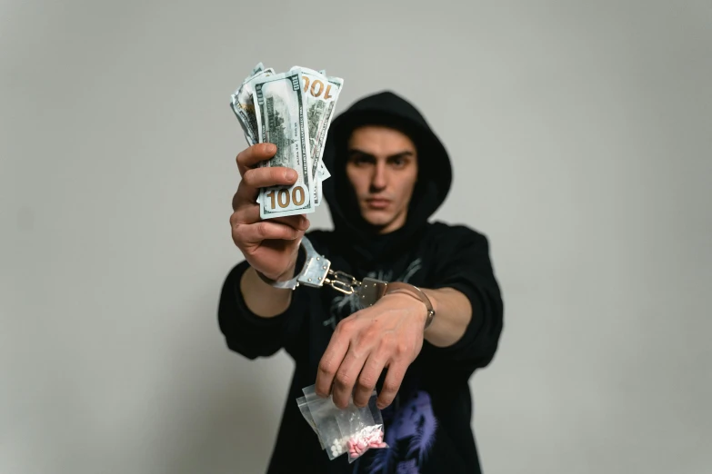 a man in a hoodie holding a bunch of money, by Niko Henrichon, pexels contest winner, hyperrealism, handcuffed, xxxtentacion, 5k, taken on iphone 14 pro