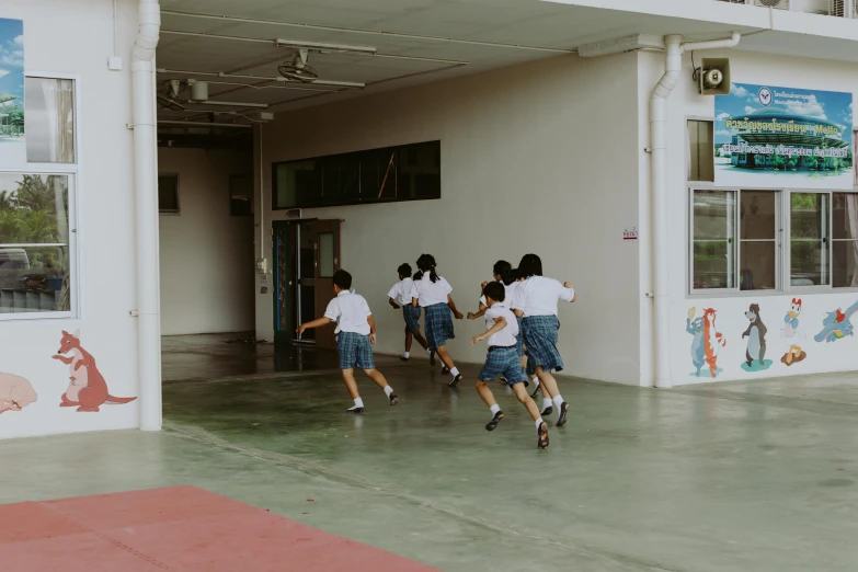 a group of children running in front of a building, inspired by Baiōken Eishun, pexels contest winner, ashcan school, in the high school gym, set on singaporean aesthetic, blank, looking at the ground