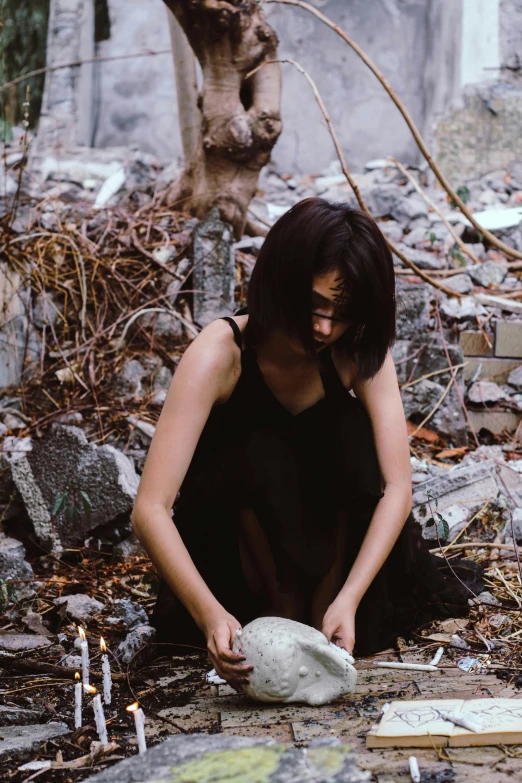 a woman sitting on the ground next to a pile of rocks, an album cover, pexels contest winner, holding a skull, asian women, disintegrating, profile image
