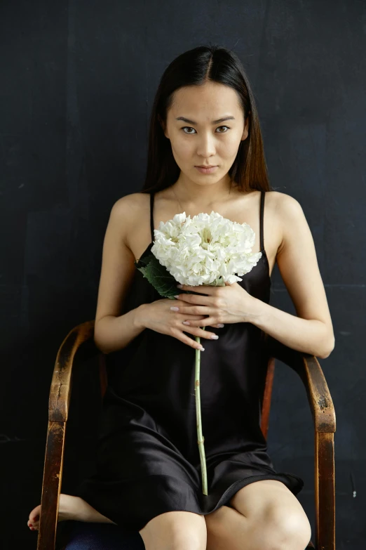 a woman sitting in a chair holding a flower, inspired by Zhang Shuqi, unsplash, neo-figurative, wearing black camisole outfit, white flowers, studio portrait, ethnicity : japanese