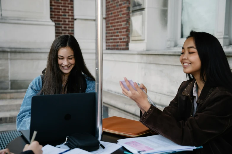 a couple of women sitting at a table with a laptop, trending on unsplash, academic art, waving, background image, exterior shot, modeled