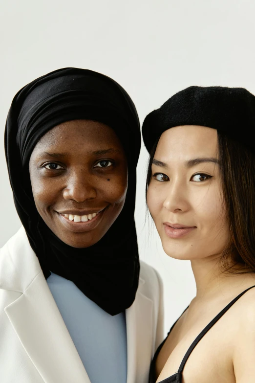 a couple of women standing next to each other, hurufiyya, natural skin tones, with black beanie on head, asian descent, black