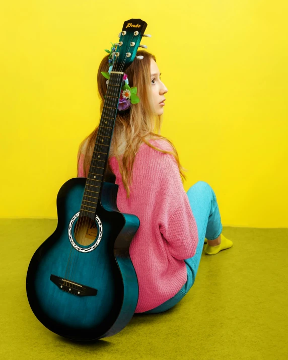 a woman sitting on the ground with a guitar, turquoise pink and yellow, nonbinary model, girl in studio, promo image