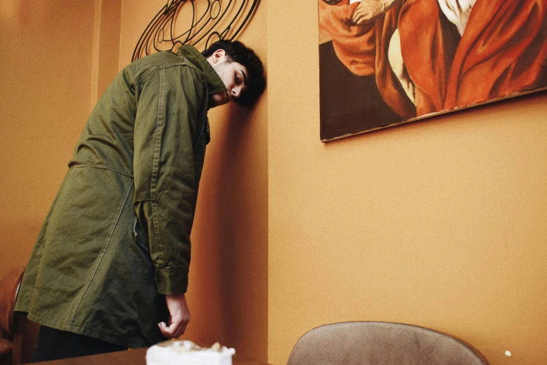 a man leaning over a table with a piece of cake in front of him, an album cover, inspired by Elsa Bleda, visual art, orange jacket, exiting from a wardrobe, weird art on the wall, impeccable military composure