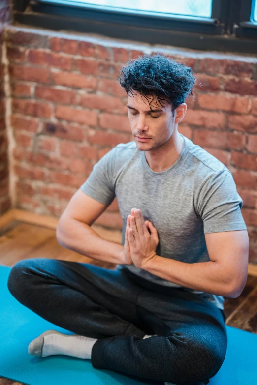 a man sitting on a yoga mat in front of a window, inspired by John Luke, sitting with wrists together, avatar image, sports clothing, mohamed chahin