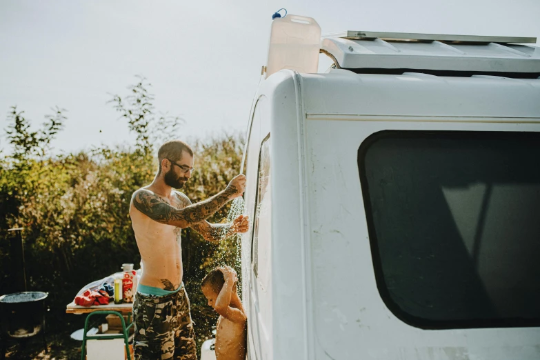 a man that is standing next to a van, by Lee Loughridge, pexels contest winner, renaissance, father with child, leaking, glamping, tattooed