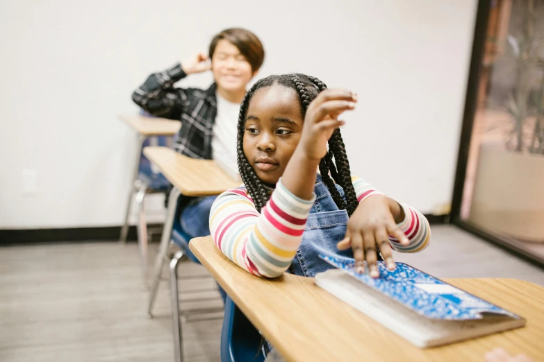 a group of children sitting at desks in a classroom, by Dan Frazier, pexels contest winner, medium shot of two characters, black teenage girl, sideways glance, holding it out to the camera