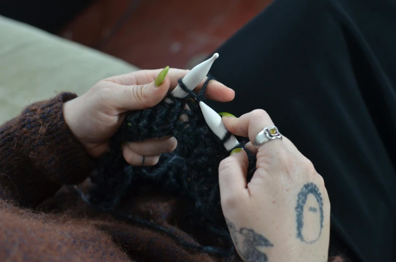 a woman sitting on a couch with a pair of scissors in her hand, a tattoo, by Jessie Algie, unsplash, process art, made out of wool, digesting a small dragon, medium close up, crochet skin