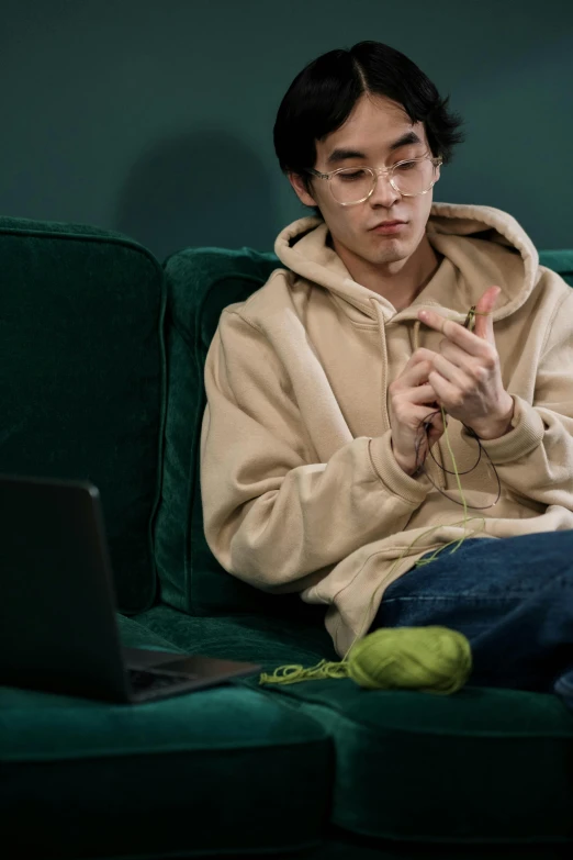 a man sitting on a couch with a laptop, inspired by Liam Wong, trending on pexels, hyperrealism, giving the middle finger, wearing a green sweater, john carmack, dressed with long fluent clothes