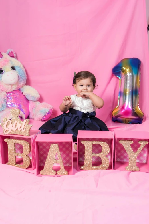 a baby girl sitting in front of a pink backdrop, a picture, happening, cubes on table, glitter accents on figure, celebration, blue themed