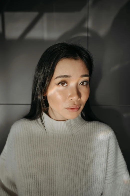 a woman standing in front of a black wall, a character portrait, inspired by Ruth Jên, trending on pexels, hyperrealism, wearing a white sweater, li bingbing, smooth symmetrical chin, indoor picture