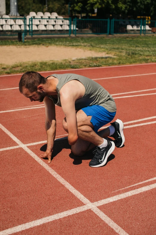 a man getting ready to run on a track, a portrait, by Carey Morris, unsplash, rectangle, kneeling, low quality photo, brown