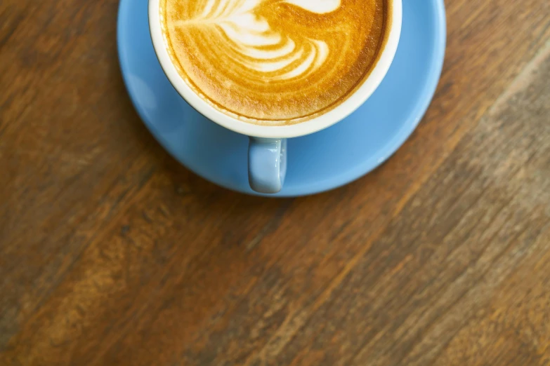 a cup of coffee sitting on top of a blue saucer, on a wooden table, 9 9 designs, thumbnail, widest shot