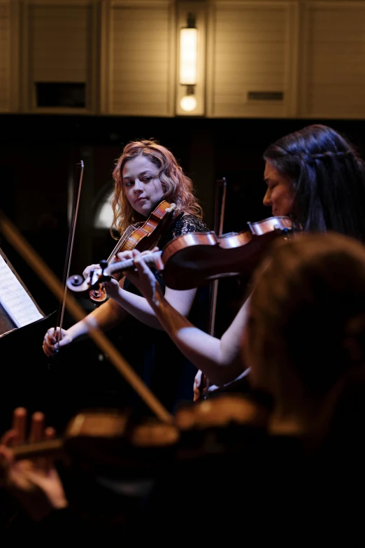 a group of people playing musical instruments in a room, standing on top of a violin, in the evening, square, sydney hanson