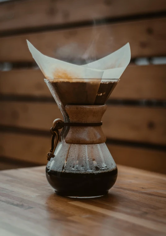 a coffee maker sitting on top of a wooden table, by Cafer Bater, pexels contest winner, parchment paper, hour glass, gif, cone shaped