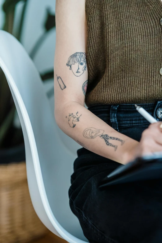 a woman sitting in a chair writing on a piece of paper, a tattoo, trending on pexels, holding arms on holsters, doodles, eva elfie, temporary tattoo