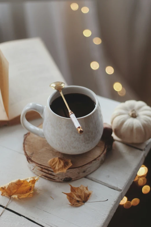 a cup of coffee sitting on top of a wooden table, by Elaine Hamilton, trending on pexels, romanticism, long trunk holding a wand, 🍂 cute, white and gold color palette, tea