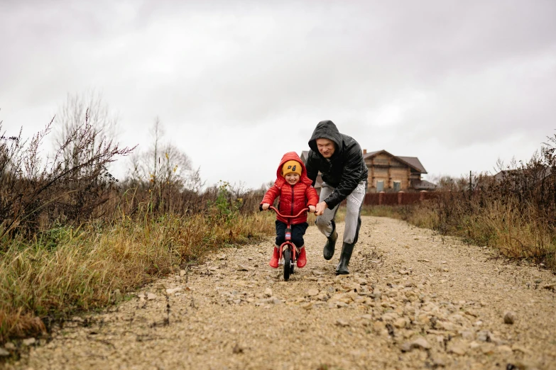 a man teaching a child how to ride a bike, a picture, by Jesper Knudsen, pexels contest winner, overcast weather, avatar image, full body image, on a farm