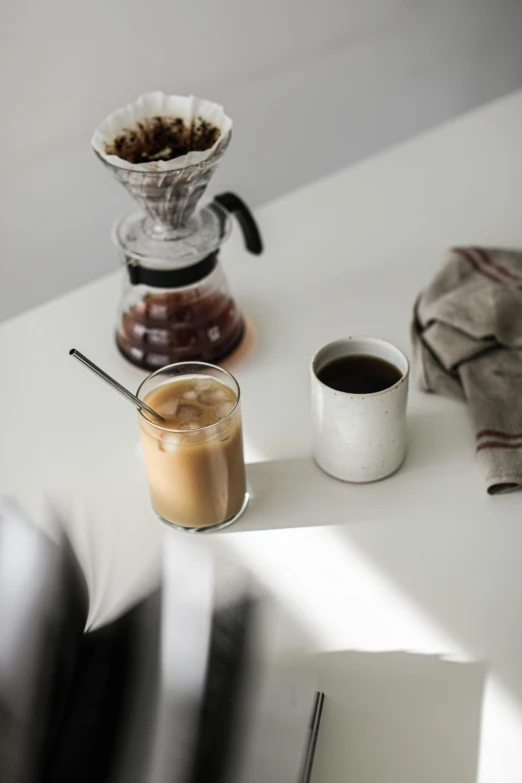 a white table topped with two cups of coffee, glassware, cold brew coffee ), stainless steal, nordic