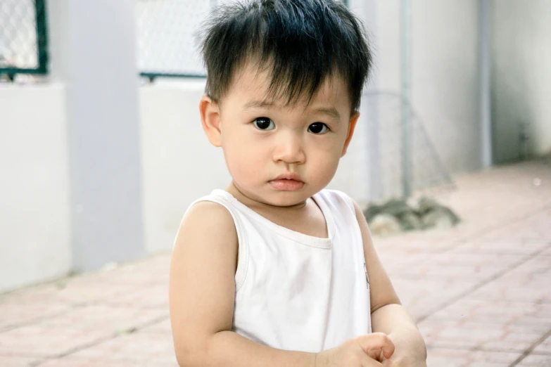 a close up of a child holding a tennis racquet, by Bernardino Mei, pexels contest winner, photorealism, wearing a tanktop, young cute wan asian face, pout, 2 years old