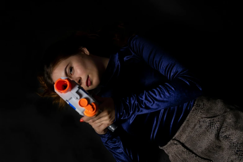 a close up of a person holding a toy gun, by irakli nadar, pexels contest winner, mara jade skywalker, sleepy, halloween, some orange and blue