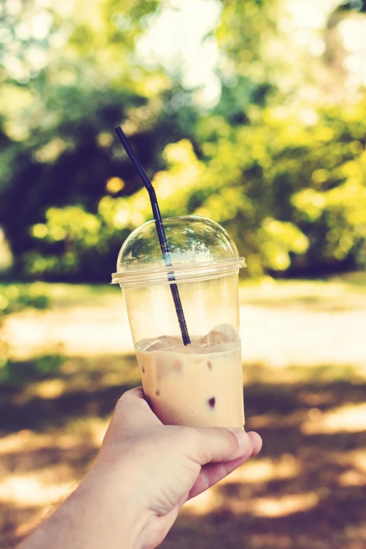 a person holding a cup of iced coffee, by Lucia Peka, sunny day in a park, instagram post, manuka, istock