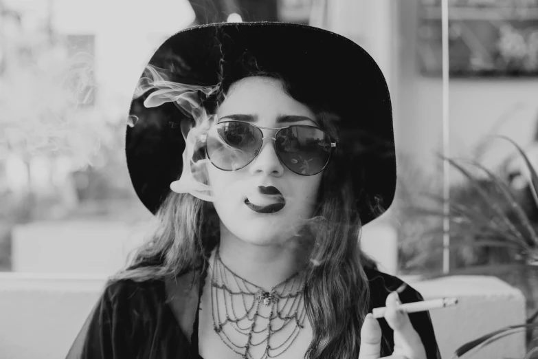 a black and white photo of a woman smoking a cigarette, a black and white photo, inspired by Evaline Ness, pexels contest winner, lowbrow, wearing sunglasses and a hat, young beautiful hippie girl, halloween, resembling a mix of grimes