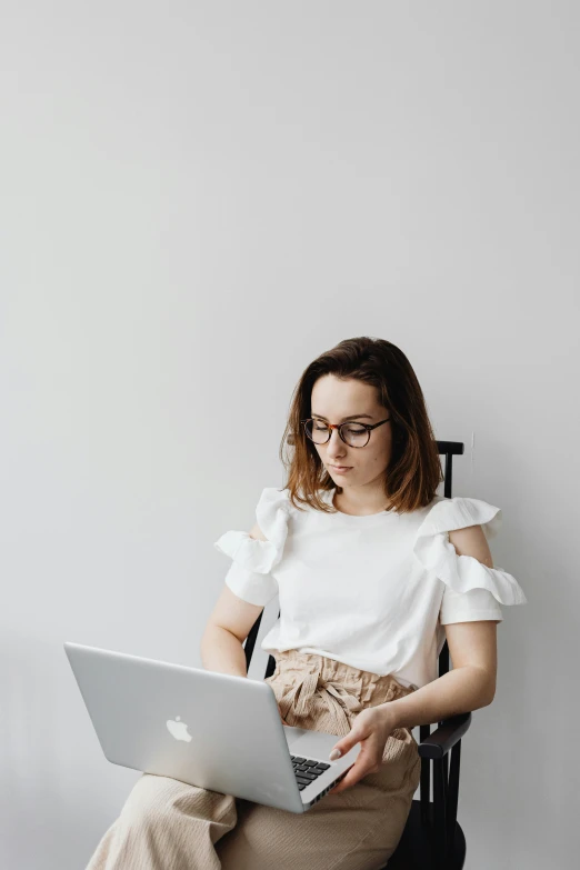 a woman sitting in a chair with a laptop, trending on pexels, dressed in a white t shirt, nerdy, wearing a designer top, detailed professional