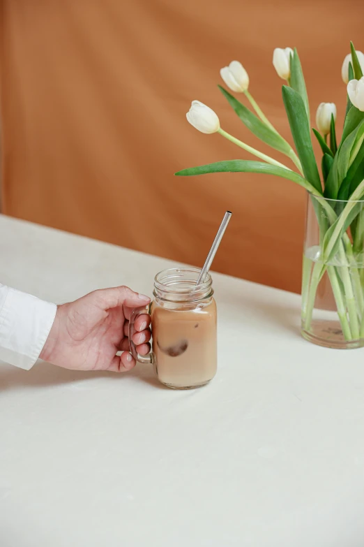 a person holding a cup of coffee next to a vase of tulips, iced latte, made of brushed steel, with a straw, product image