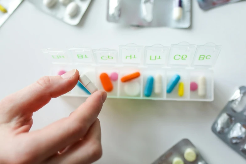 a close up of a person holding a pill case, by Rachel Reckitt, pexels, antipodeans, ingredients on the table, various colors, ultra - realistic, medical labels