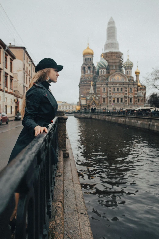 a woman standing on a bridge next to a river, by Serhii Vasylkivsky, pexels contest winner, baroque, domes, streetwear, tall hat, towering over a city