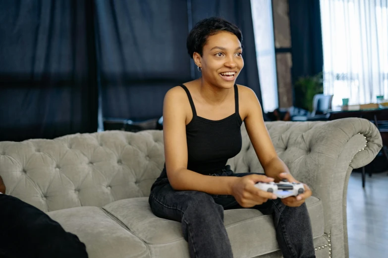 a woman sitting on a couch holding a video game controller, pexels contest winner, happening, black young woman, wearing a black cropped tank top, avatar image, delightful surroundings