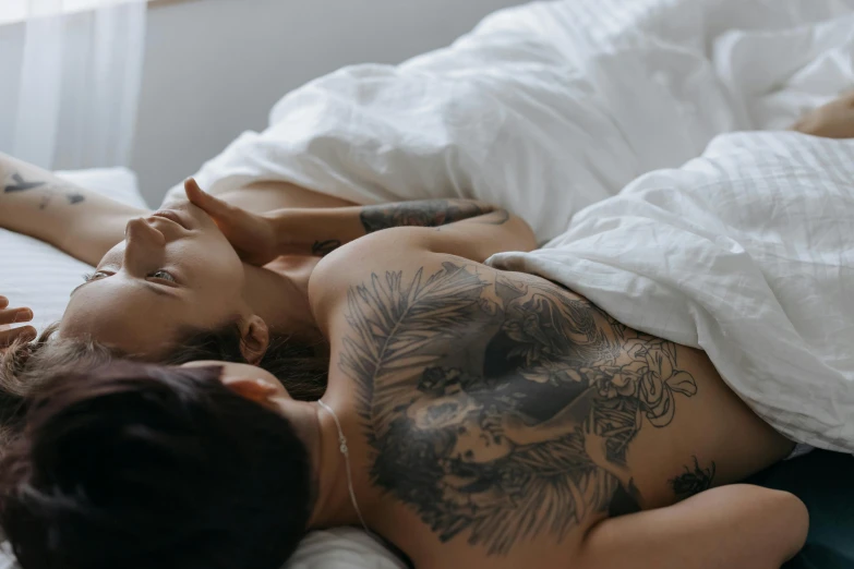 a woman laying on top of a bed next to a man, a tattoo, trending on pexels, lesbian embrace, gif, sydney hanson, facing each other