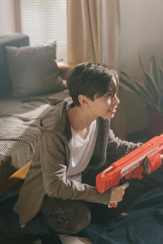 a boy is sitting on the floor with a toy gun, pexels contest winner, energy rifle, red and orange colored, at home, hyperrealistic teen