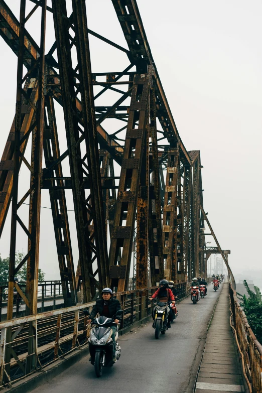 a group of people riding motorcycles across a bridge, vietnam, red trusses, rust, 🚿🗝📝