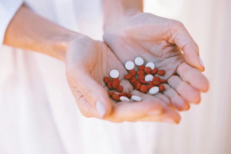 a person holding a handful of pills in their hands, by Emma Andijewska, unsplash, antipodeans, silver red white details, on a wooden tray, rabies, 15081959 21121991 01012000 4k