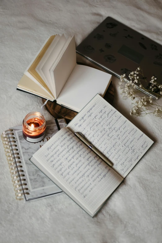 an open book sitting on top of a bed next to a candle, pexels, writing on a clipboard, three quater notes, on a pale background, spiraling