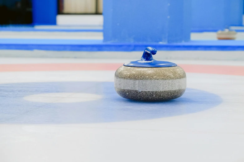 a curling stone sitting on top of an ice rink, inspired by Muirhead Bone, dipped in polished blue ceramic, thumbnail, grey, mid shot