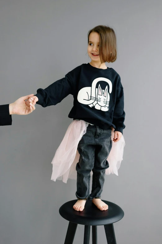 a little girl standing on top of a stool, a cartoon, unsplash, graffiti, wearing a black sweater, cat tail, official product photo, 5 fingers). full body