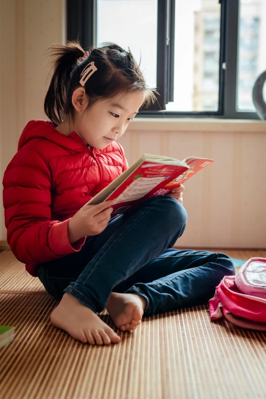 a little girl sitting on the floor reading a book, pexels contest winner, wearing red clothes, educational supplies, lulu chen, wearing a pink hoodie