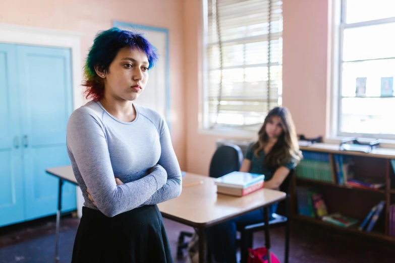 a woman with colorful hair standing in front of a desk, by Arabella Rankin, trending on pexels, renaissance, in a school classroom, lesbian, looking sad, two girls