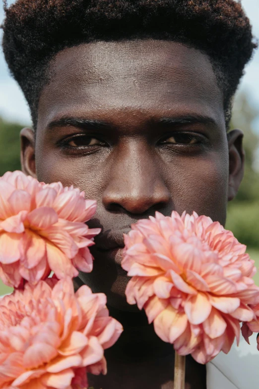 a man holding flowers in front of his face, by Carey Morris, trending on unsplash, brown skinned, non binary model, dahlias, in shades of peach